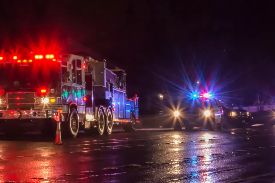 Nighttime view of fire truck and police cars with flashing lights on parked in a wet street